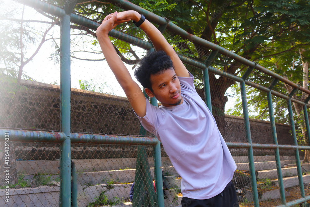 Fototapeta premium A man is stretching his arm in front of a fence. Concept of determination and focus as the man works on his flexibility