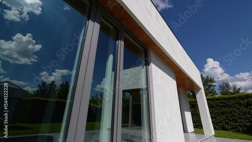 Wallpaper Mural Modern minimalist home exterior featuring large glass windows, white facade, clean lines, green lawn, lush garden, and natural sunlight under blue sky Torontodigital.ca