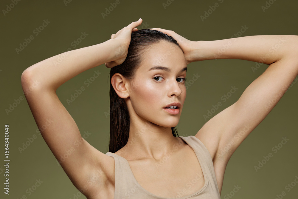 Fototapeta premium Young woman with sleek hair holding her head in a serene pose against a green backdrop, showcasing natural beauty and healthy hair care
