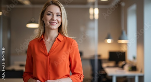 Portrait of a smiling blonde woman in an office wearing an orange shirt