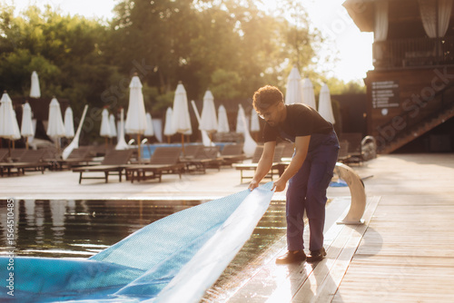 Wall Mural Pool maintenance worker removing solar cover at resort in the morning