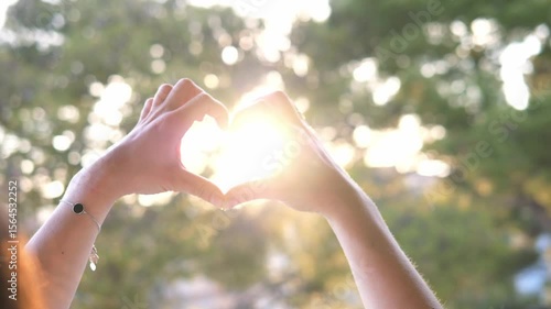 A woman's heart-shaped hands reach out to the sun, catching its warm light.