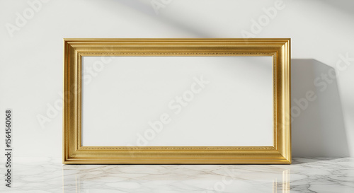 A golden rectangular picture frame leans against a textured white wall.