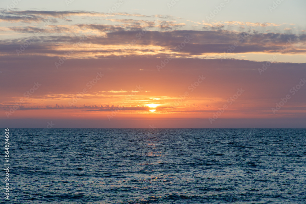 Obraz premium The sun is setting over the ocean, casting a warm glow on the water