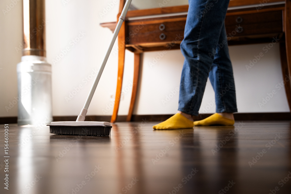 Fototapeta premium Woman sweeping dust from the wooden floor with a rubber mop in living room at home, female using rubber floor brush for dry cleaning routine and daily household chores