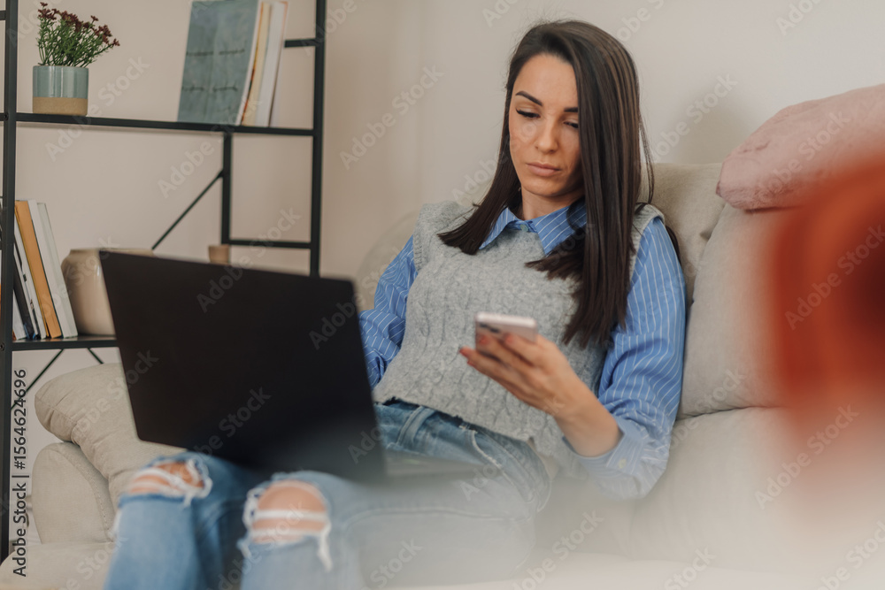 Young woman working from home using laptop and smartphone on sofa Young woman working from home using laptop and smartphone on sofa