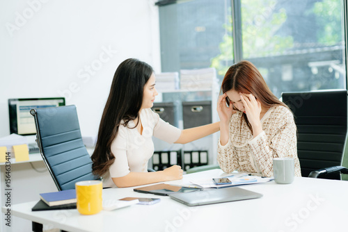 Asian woman comforts her distressed coworker in office. Concept of workplace stress, burnout, empathy, and emotional support in professional environments.