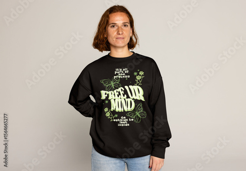 Jumper mockup. A young woman, with short hair and jeans, is posing in a plain sweatshirt against a neutral background and looking at camera.