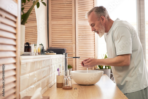 Foto Middle aged Caucasian man washing face at bathroom sink, performing daily skinca
