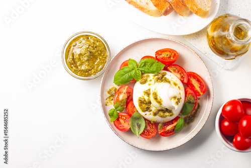 Burrata cheese caprese salad with cherry tomatoes, olive oil, pesto and seasoning. Fresh food concept. 
