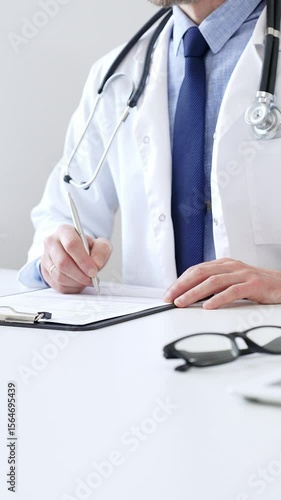 Male doctor writing a prescription and filling out medical records on a clipboard in an office setting, showcasing the essential aspects of healthcare and patient care. Medicine and health care
