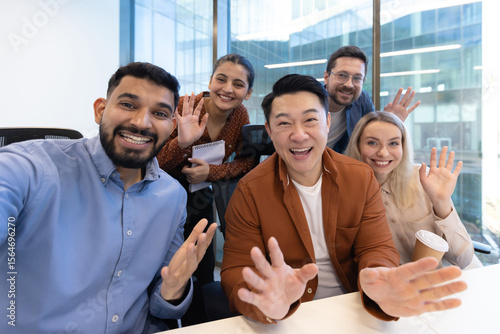 фотографія A diverse group of colleagues wave enthusiastically at the camera, creating a friendly, welcoming atmosphere in a modern office setting