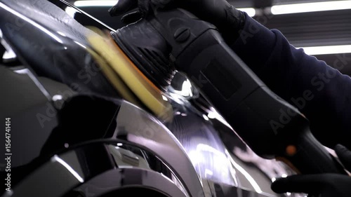 A man polishes a black car with a polishing machine in a car dealership. Car care in an auto repair shop.