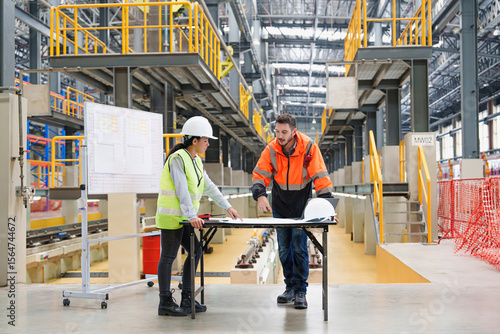 Tableau sur toile Male and female technicians reviewing rail infrastructure plans on a table