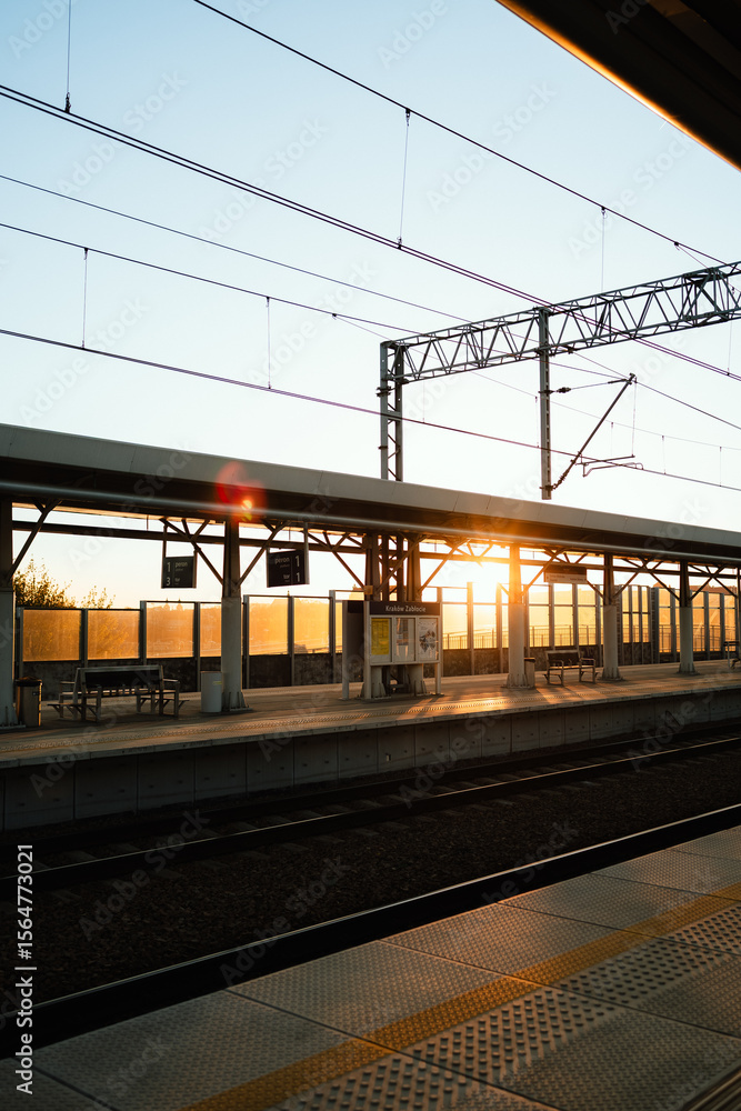 Naklejka premium Vertical screen: soft dawn illumination filtering through architectural train station interior, casting elongated shadows across empty platforms and gleaming rails. Modern train station architecture
