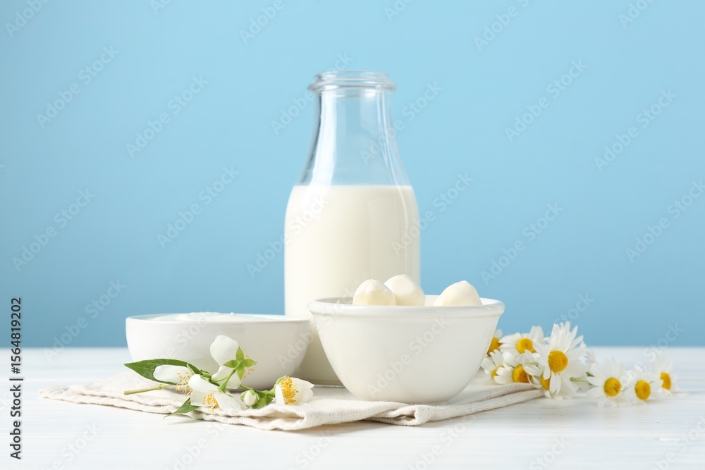 Fresh dairy products and flowers on white wooden table against light blue background Fresh dairy products and flowers on white wooden table against light blue background