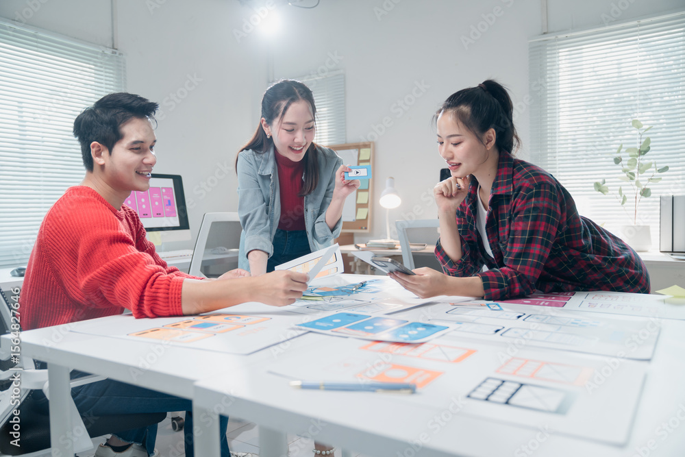 Fototapeta premium Diverse group of young professionals engaging in a collaborative design session. They are brainstorming and reviewing digital interface layouts in a modern, well-lit office space