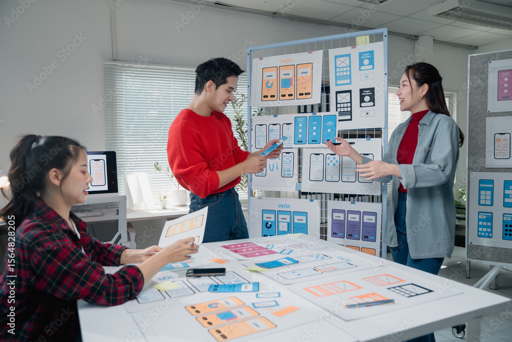 Obraz premium Creative team engaged in designing a mobile app interface, discussing layouts and features. Diverse group of professionals collaborating in a modern office setting