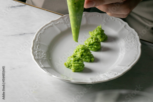 Piping vibrant pea puree rosettes, culinary artistry blooms under deft fingers, ideal for Nouveau Cuisine Day or La Tomatina