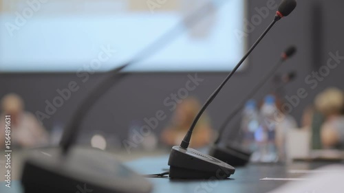Microphone is on a table in front of a projector screen. The microphone is black and the projector screen is white