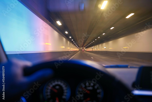 Blurred view from inside a moving car driving through a brightly lit tunnel.