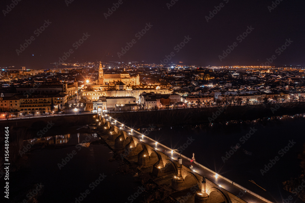 Naklejka premium An aerial view showcases the stunning Mosque-Cathedral of Cordoba, with its distinctive bell tower and surrounding courtyards, bathed at night