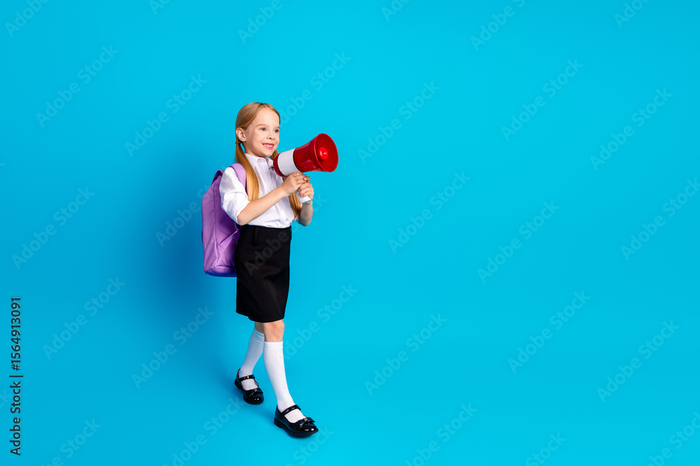 Young schoolgirl with megaphone in school uniform smiling cheerfully against a blue background, promoting education Young schoolgirl with megaphone in school uniform smiling cheerfully against a blue background, promoting education