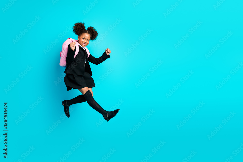 Obraz premium Confident schoolgirl jumping joyfully on a teal background to promote education, enthusiasm, and youthful vitality