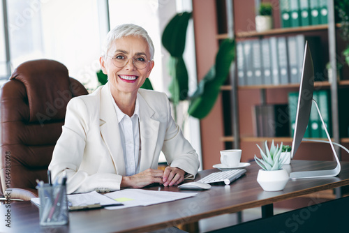 Elegant senior businesswoman smiling confidently at her modern office desk with a professional and stylish demeanor