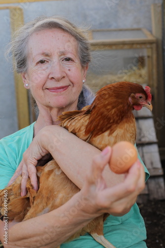 Senior female farmer holding a chicken and a fresh egg 