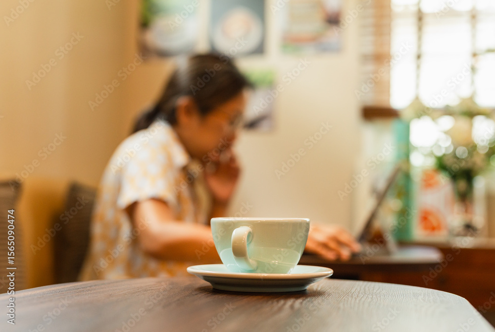 Selected focus cup of coffee on table with woman working on laptop in blur background. Selected focus cup of coffee on table with woman working on laptop in blur background.