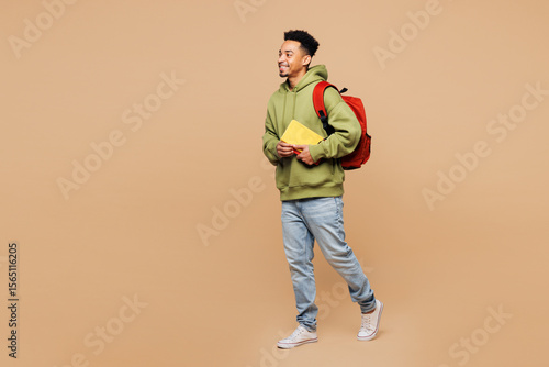 Foto Full body side view young smart boy student wearing green casual clothes backpack bag hold books walking going isolated on plain pastel light beige background