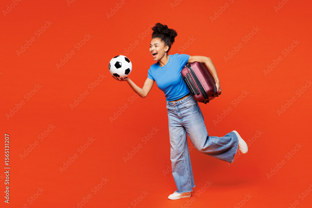 Full body young tourist woman fan wear basic blue t-shirt cheer up support football sport team hold suitcase soccer ball watch tv live stream travel abroad run isolated on plain red orange background. Full body young tourist woman fan wear basic blue t-shirt cheer up support football sport team hold suitcase soccer ball watch tv live stream travel abroad run isolated on plain red orange background.