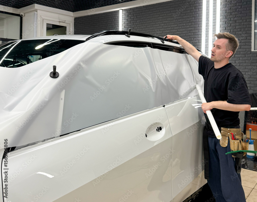A car wrapping specialist applies a polyurethane film to the car. Detailer smoothes PPF. Car wrapping, detailing, tuning and styling. Selective focus. PPF protective film against chips and scratches. A car wrapping specialist applies a polyurethane film to the car. Detailer smoothes PPF. Car wrapping, detailing, tuning and styling. Selective focus. PPF protective film against chips and scratches.