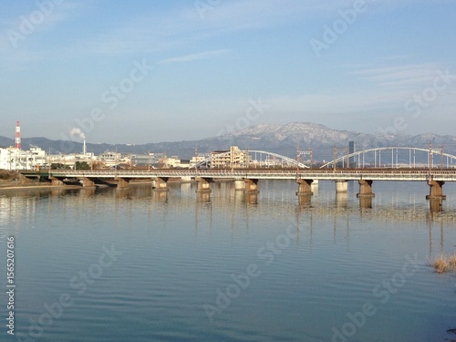 Photography A beautiful reflection of a truss bridge and the snow-capped Mount Ibuki in the calm Kiso River, Japan