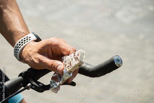 Energy or protein bar in cyclist hand. Man snacks and riding bike. Healthy protein snack or energy bar for sporty lifestyle. Close up