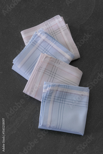 Folded blue and beige handkerchiefs arranged on a dark background, showcasing classic men's accessories in a clean, elegant style.