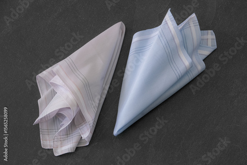 Folded blue and beige handkerchiefs arranged on a dark background, showcasing classic men's accessories in a clean, elegant style.