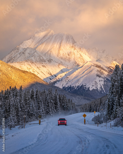 Red car driving on snowy road at sunrise in Kananaskis Country