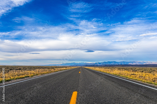 Long empty road stretching through Idaho desert landscape under cloudy blue sky