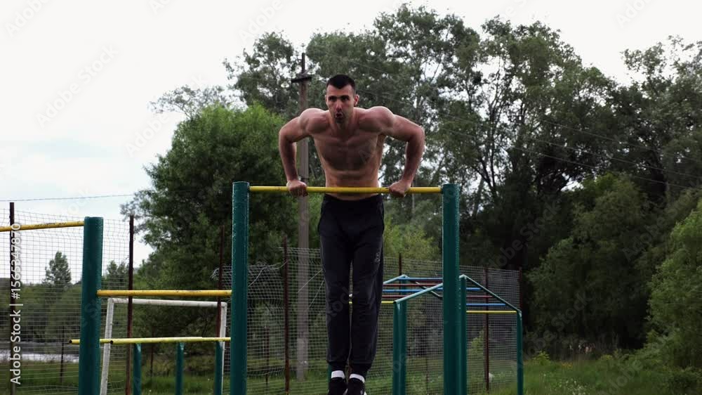 Hardy shirtless sportsman doing push ups on horizontal bar at nature. Strong and muscular guy training at sports ground. Young athletic guy exercising outdoor. Concept of active and healthy lifestyle Hardy shirtless sportsman doing push ups on horizontal bar at nature. Strong and muscular guy training at sports ground. Young athletic guy exercising outdoor. Concept of active and healthy lifestyle
