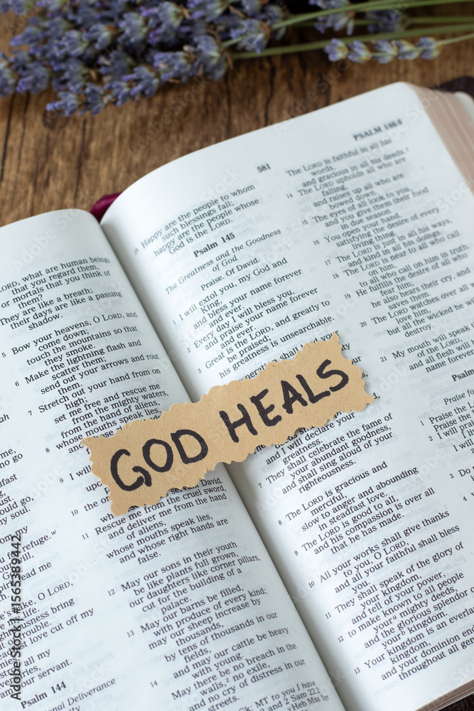 Fototapeta premium God heals handwritten text note on open holy bible book. Top view. Christian restoration and encouragement, biblical concept.