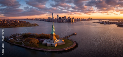Aerial panorama of the Statue of Liberty in front of Jersey City and New York City skylines at sunset.