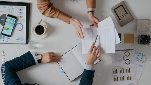 View from above of two unrecognisable business partners discussing contract and shaking hands after reaching agreement at white work table