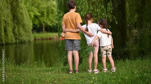 Three Young Children Embrace by the Lake, Enjoying Nature's Beauty and Each Other's Company.