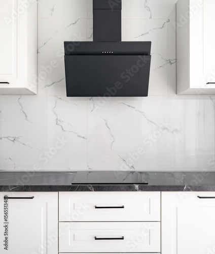 Black range hood on a white modern kitchen with marble backsplash, black induction cooktop and white cabinets