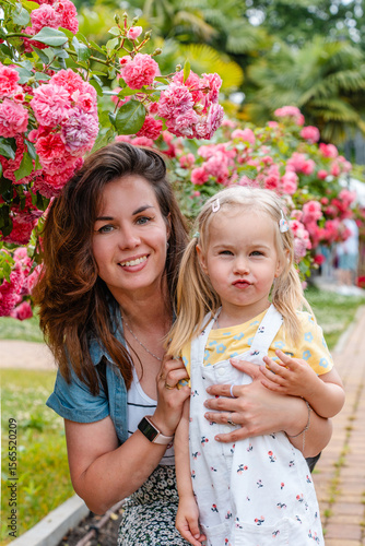 Child girl with her mother in a blooming garden with bushes of roses and flowers