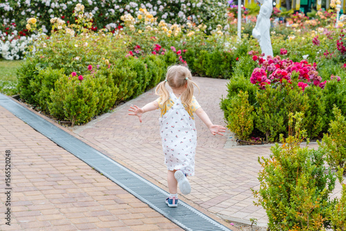 Child girl runs in a blooming garden with bushes of roses and flowers
