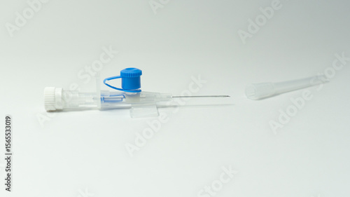 Photos IV cannula with blue valve and exposed needle placed next to its transparent protective cap on a white background