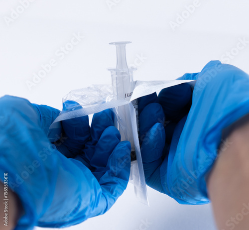 Close-up of gloved hands opening the sterile packaging of a disposable syringe. Essential preparation step in clinical, hospital, or pharmaceutical environments.